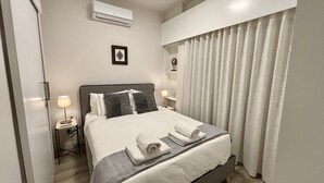 Un lit bien fait, avec du linge de lit blanc et deux oreillers, une lampe de chevet, une petite table de chevet et un cadre photo accroché au mur.