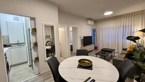 Un salon moderne avec une table à manger ronde, des chaises grises, un téléviseur à écran plat et une grande fenêtre agrémentée de rideaux.