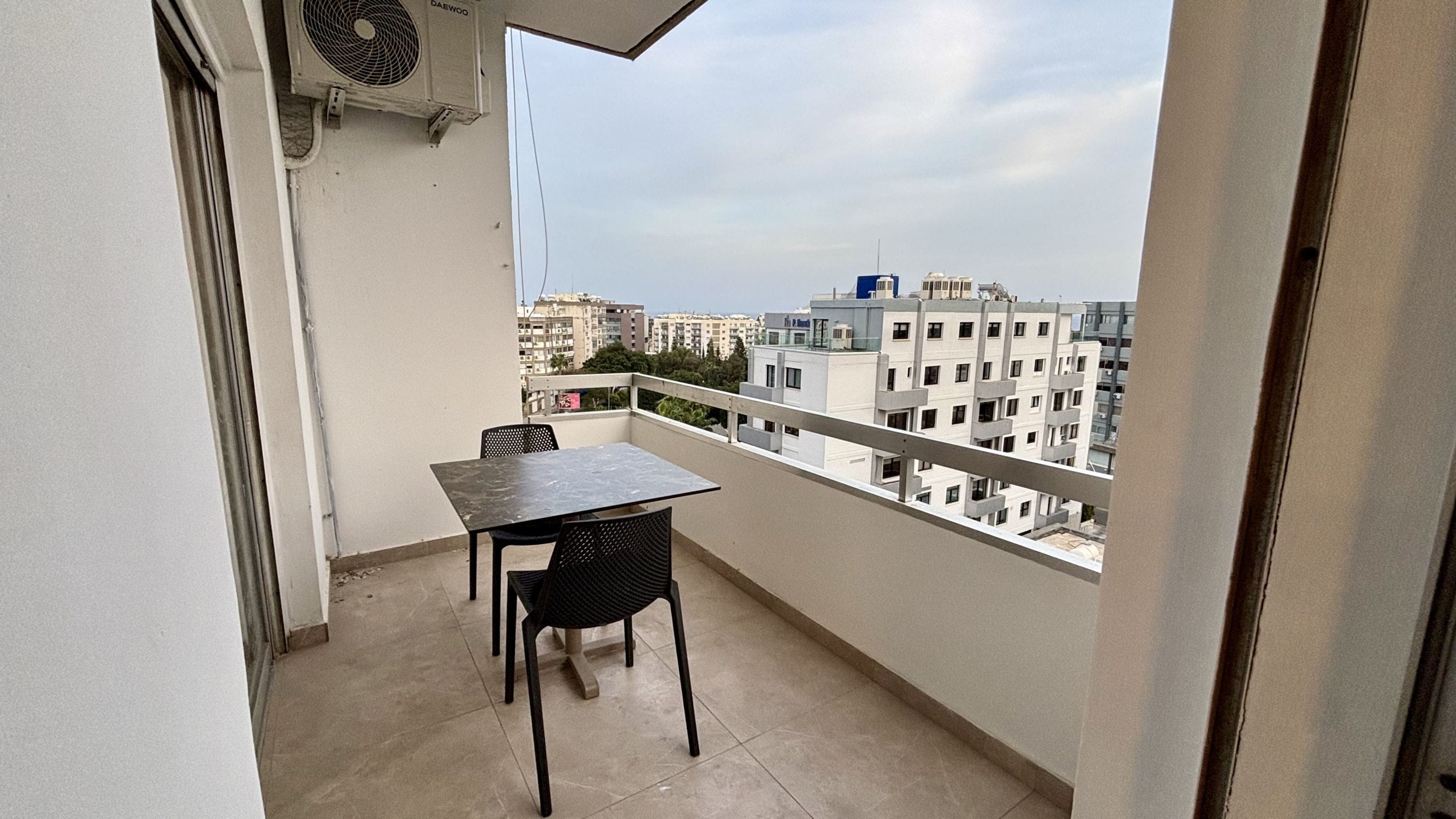 A balcony with a table and chairs, overlooking a cityscape with multiple buildings.