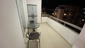 Un balcon avec une table et des chaises, une porte et une vue sur la ville la nuit.
