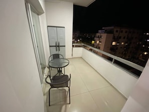 Ein Balkon mit Tisch und Stühlen, einer Tür und Blick auf die nächtliche Stadt.
