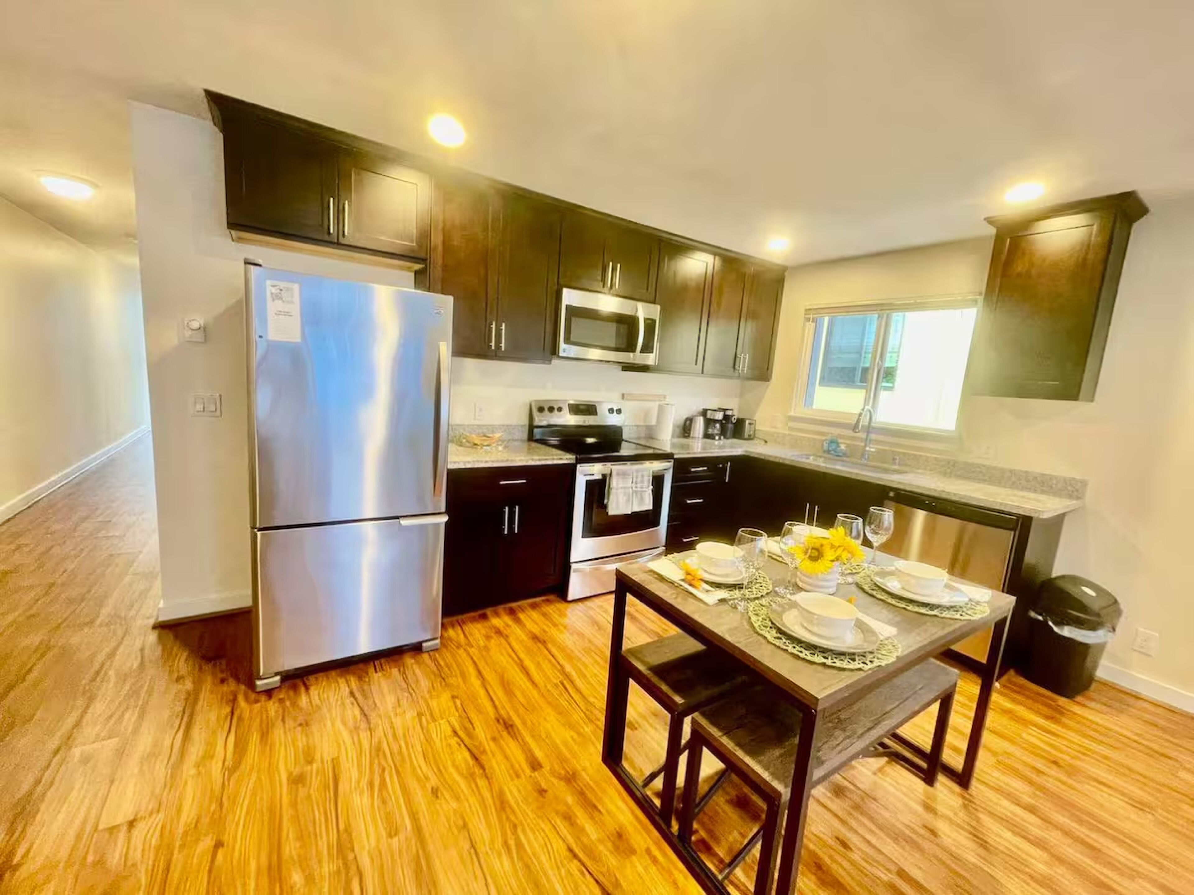 A modern kitchen with dark wood cabinets, stainless steel appliances, and a wooden dining table set for four.