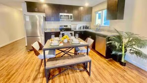 A modern kitchen with dark cabinets, stainless steel appliances, and a dining area with a wooden table and chairs. - The Seattle Haven - Modern Suites (Seattle)