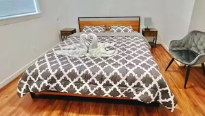 A neatly made bed with a patterned bedspread, two bedside tables with lamps, a chair, and a window with blinds. - The Seattle Haven - Modern Suites (Seattle)