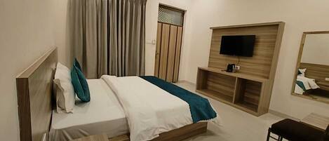 A modern bedroom with a bed, bedside table, TV, and a small seating area.