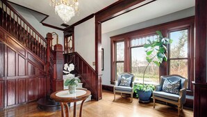 A spacious room with a wooden staircase, a chandelier, and two sofas with potted plants. - Rosedale at Historic Hopffgarten House (Boise)