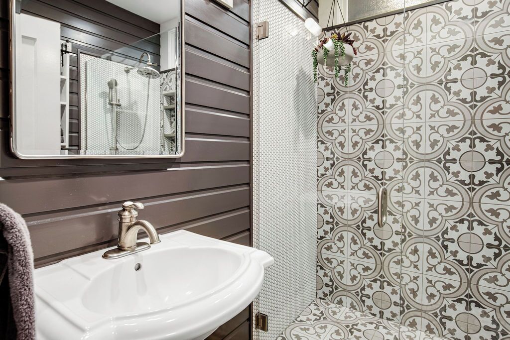 A bathroom with a white sink, a mirror, and patterned tiles.