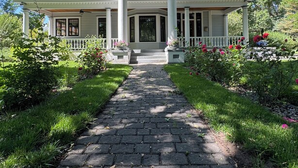 A two-story house with a central entrance, a covered porch, and a garden with flowers and a pathway leading to the entrance. - Rosedale at Historic Hopffgarten House (Boise)
