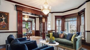 A spacious living room with a green sofa, blue armchairs, and a chandelier. - Rosedale at Historic Hopffgarten House (Boise)