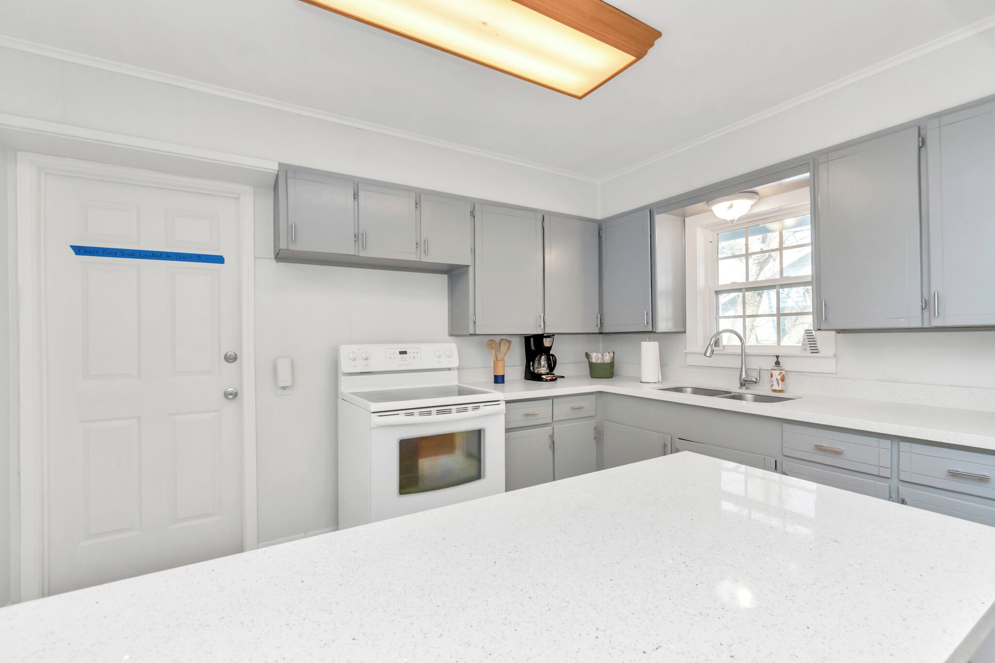 Une cuisine moderne avec des meubles blancs, un grand îlot central et une fenêtre qui laisse entrer la lumière naturelle.