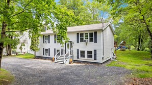A two-story house with a front porch, a staircase, and a playground in the background. - Hot Tub*Arcade*Pool Table*King Bed*75" TV*Fire Pit (Pocono Summit)