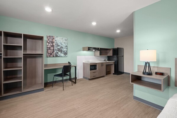 Une chambre d’hôtel moderne équipée d’une kitchenette, d’un bureau, d’une chaise et d’une table de chevet avec une lampe.