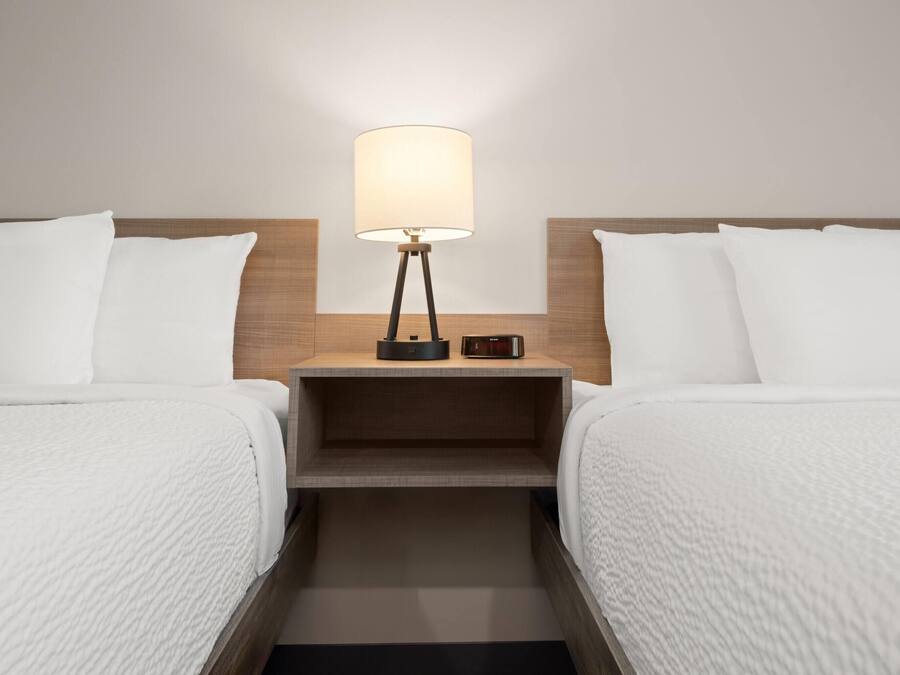 Ein Hotelzimmer mit zwei Betten, einem Nachttisch mit Lampe und einem kleinen Tisch.