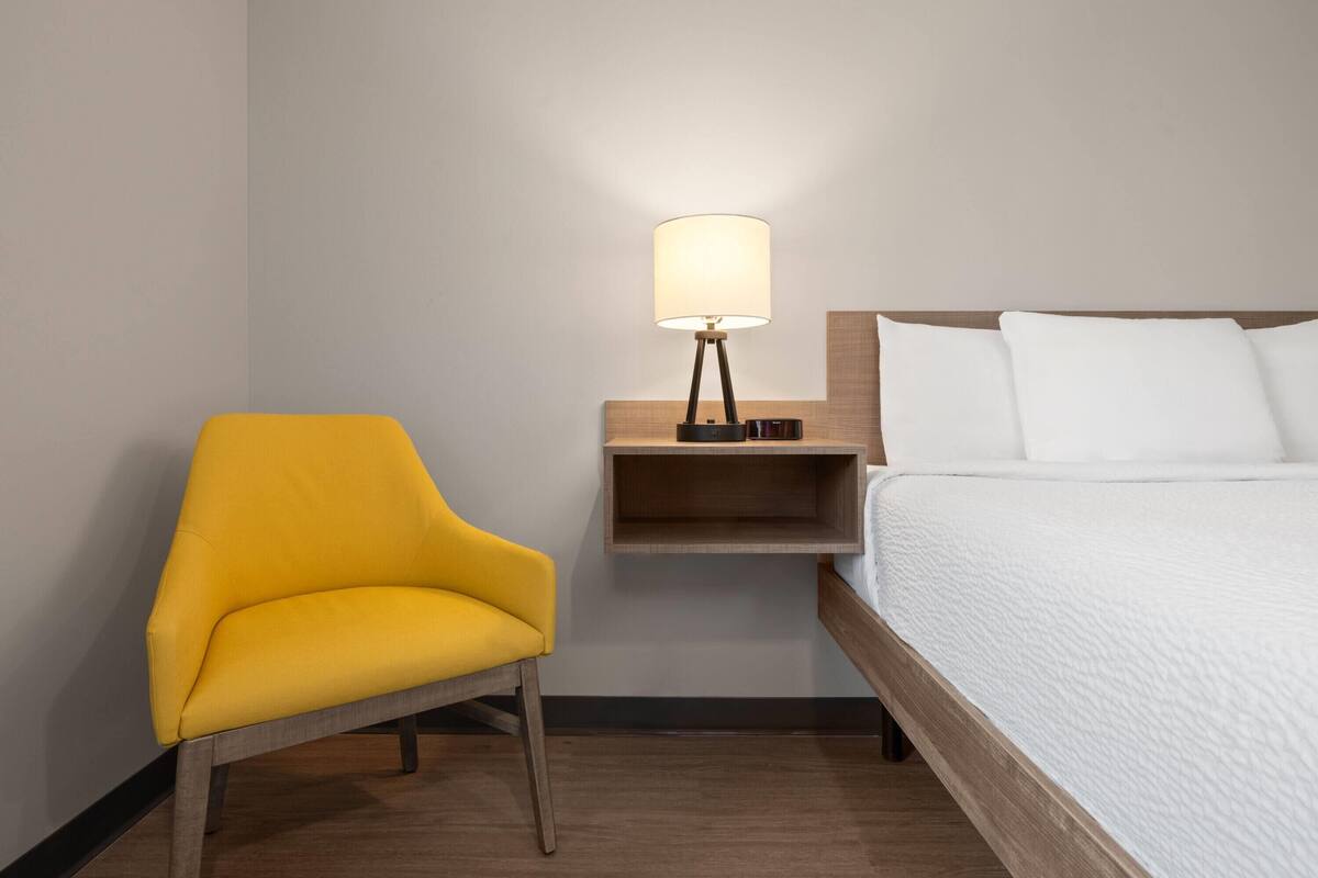 A hotel room with a single bed, a bedside table with a lamp, and a yellow armchair.