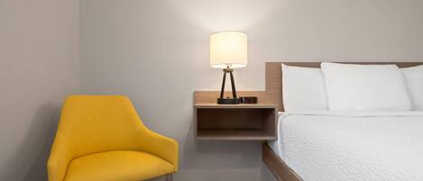 Quarto de hotel com uma cama de solteiro, uma mesa de cabeceira com abajur e uma poltrona amarela.