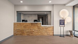 A reception area with a wooden reception desk, a glass partition, and a wall-mounted sign. - Echo Suites Extended Stay By Wyndham Johnson City Medical Cr (Johnson City)