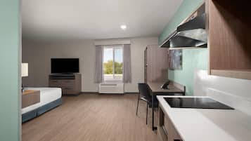 Une chambre d’hôtel moderne équipée d’un lit, d’un bureau, d’une chaise, d’une télévision et d’une kitchenette.