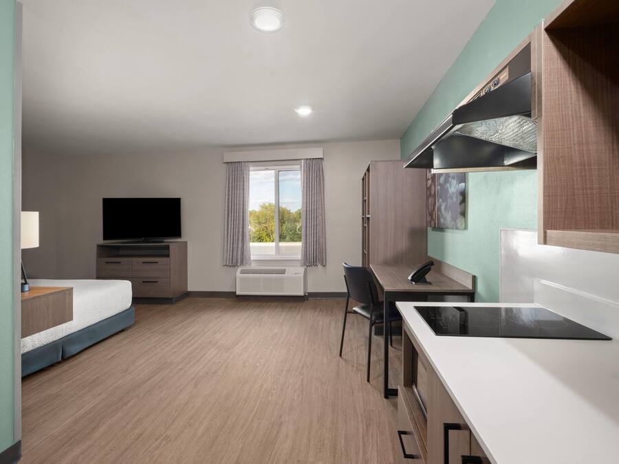Une chambre d’hôtel moderne équipée d’un lit, d’un bureau, d’une chaise, d’une télévision et d’une kitchenette.