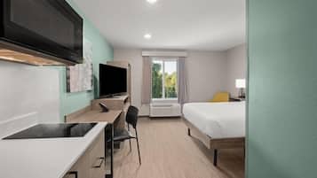 Una habitación de hotel con kitchenette, una cama, un escritorio y un televisor.