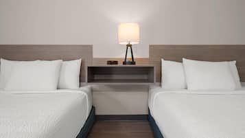 A hotel room with two beds, a nightstand with a lamp, and a shelf with a clock.