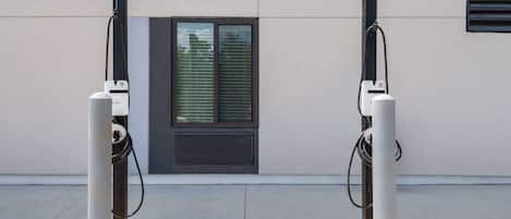 Two electric vehicle charging stations mounted on a building facade with a window and ventilation grilles.