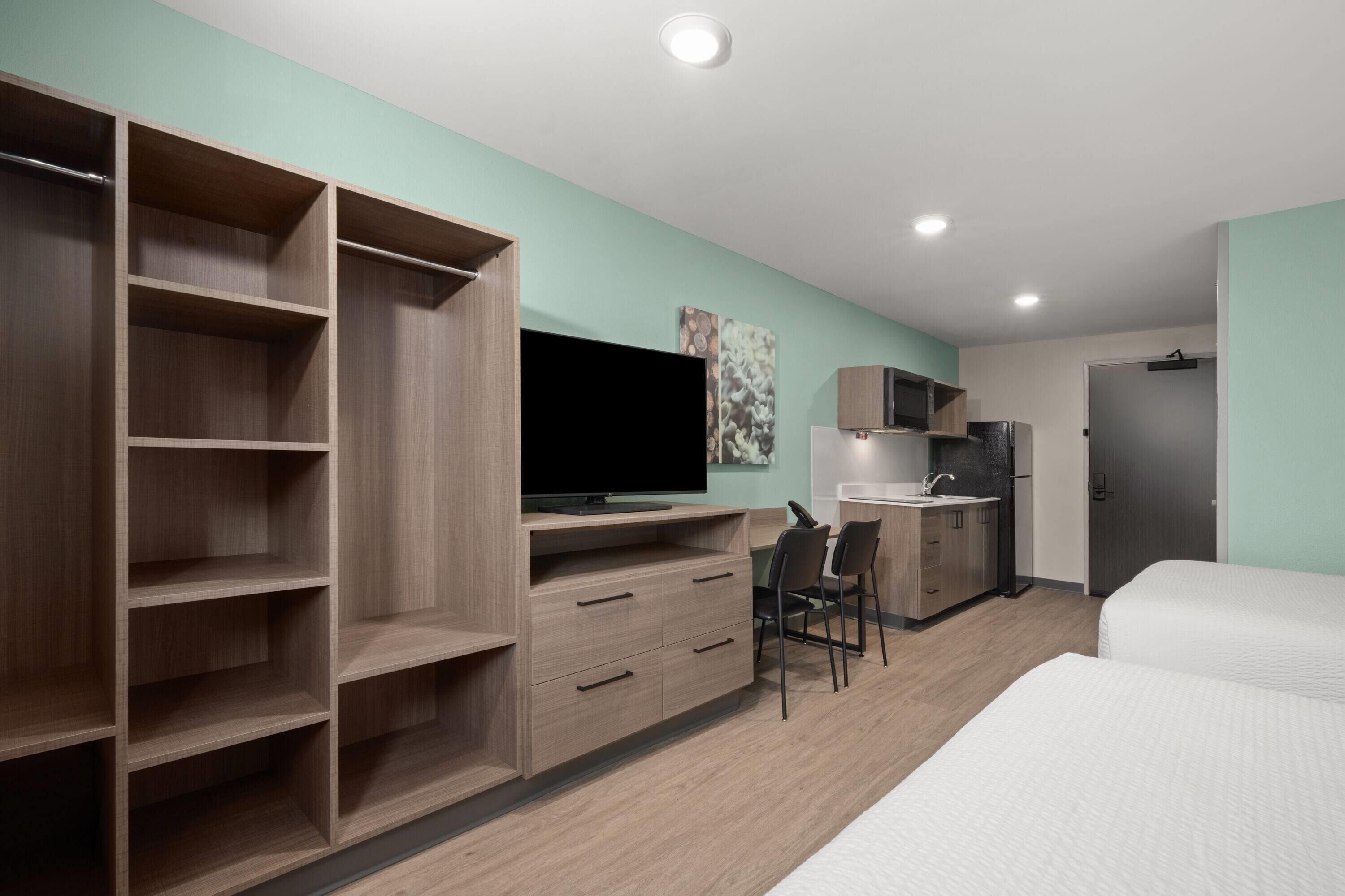 Habitación de hotel moderna con un armario grande, televisor de pantalla plana, escritorio con silla, cama y kitchenette.