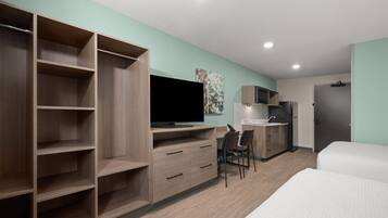 Habitación de hotel moderna con un armario grande, televisor de pantalla plana, escritorio con silla, cama y kitchenette.
