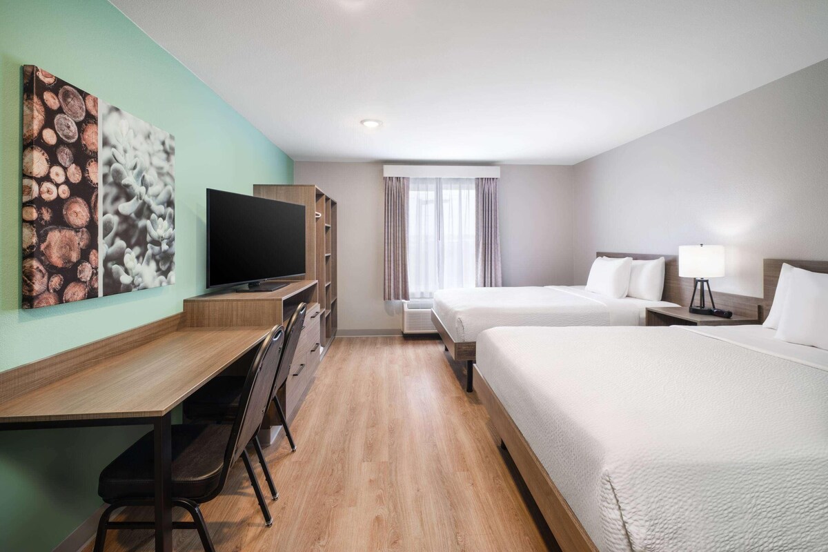 A hotel room with a wooden desk, a television, two beds, and a window with curtains.
