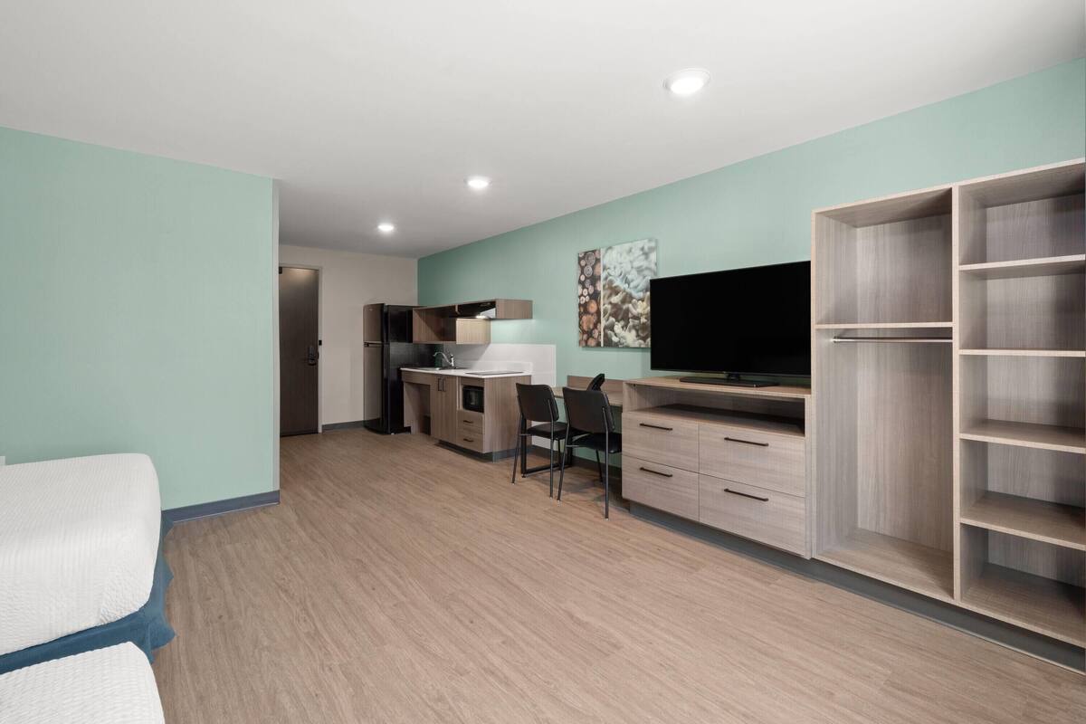 A modern room with a kitchenette, a TV, a desk, and a wardrobe.