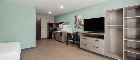 Una habitación moderna con kitchenette, televisor, escritorio y armario.