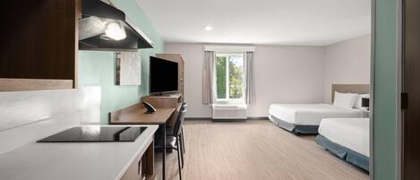 A hotel room with a desk, two beds, a TV, and a window with curtains.