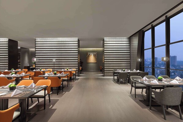 A modern dining area with tables and chairs, large windows, and a city view.