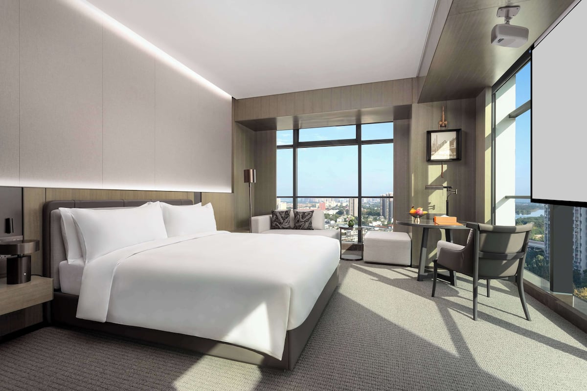 A modern hotel room with a large bed, a desk, and a view of the city.