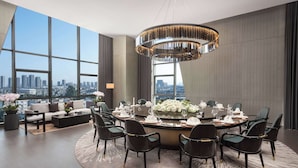 A modern dining area with a round table set for six, surrounded by dark chairs. A large chandelier hangs from the ceiling, and the room features large windows offering a city view. - Wyndham Grand Chengdu East (Chengdu)