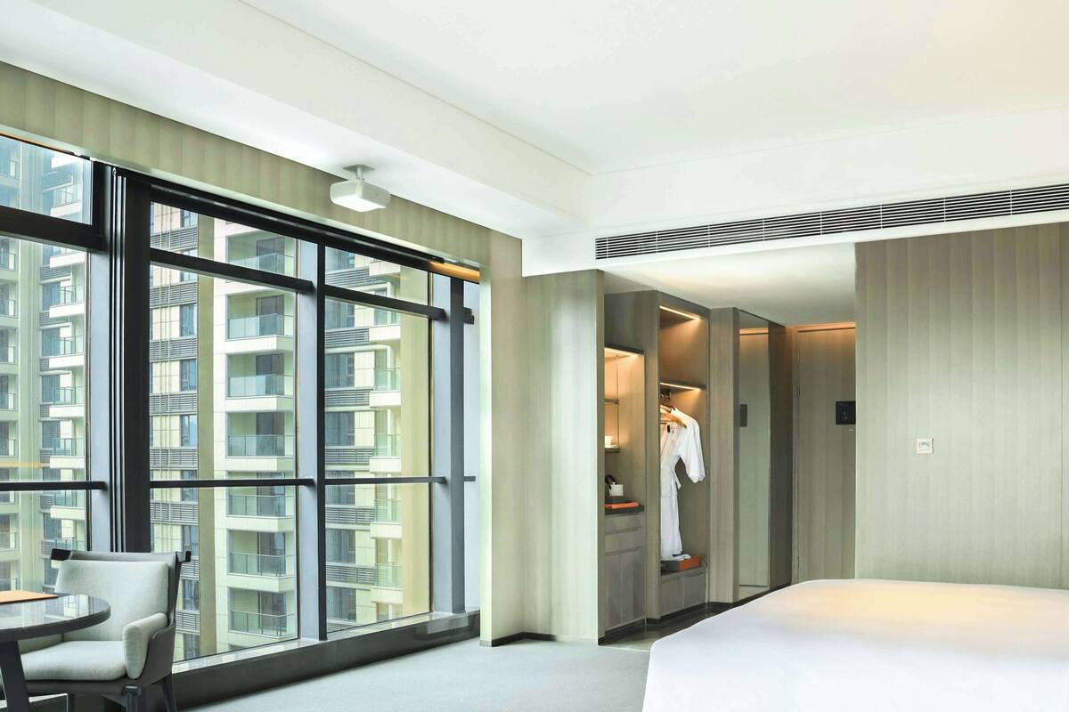A hotel room with a large window, a bed, a chair, and a walk-in closet.
