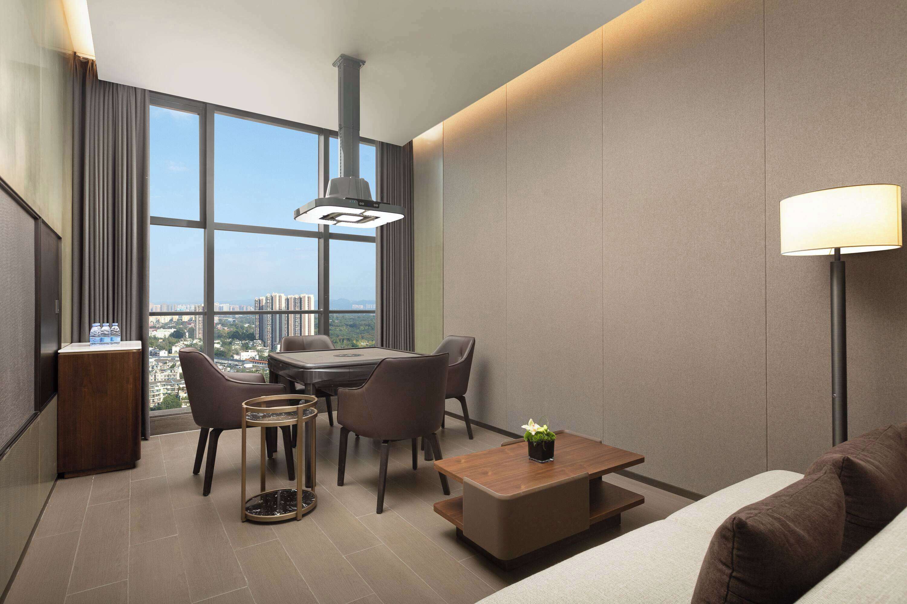 Una habitación de hotel moderna con comedor, sofá, una mesa de centro y un amplio ventanal con vistas a la ciudad.