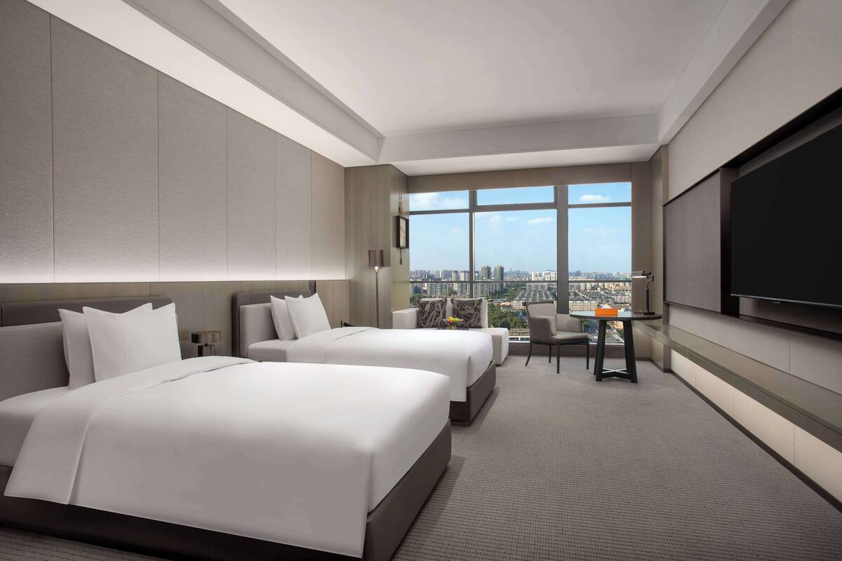A modern hotel room with two beds, a desk, and a large TV.