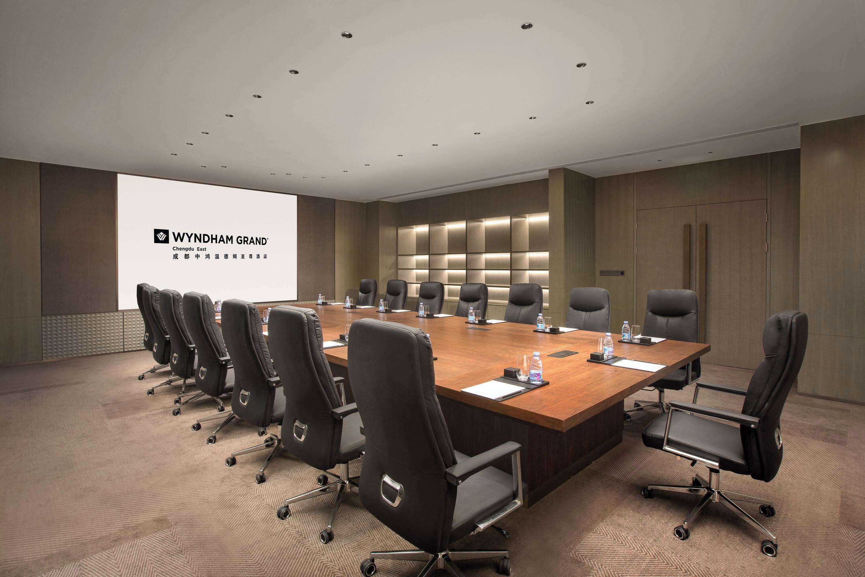 Uma sala de conferências com uma mesa comprida, cadeiras pretas e uma tela de apresentação.