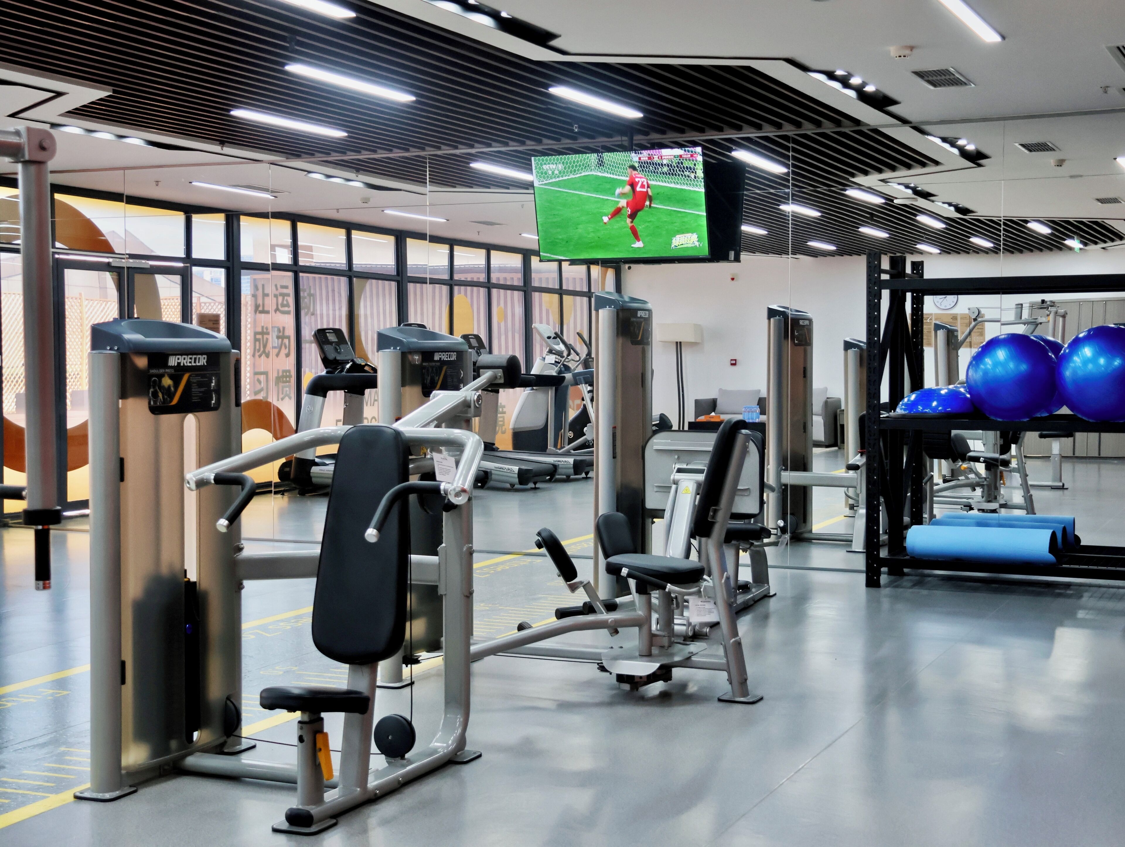 A gym with exercise equipment, a television screen, and a wall with windows.