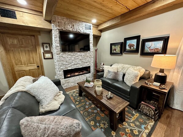 Cozy living room with a fireplace, sofa, and coffee table, featuring wooden beams and framed pictures on the wall.