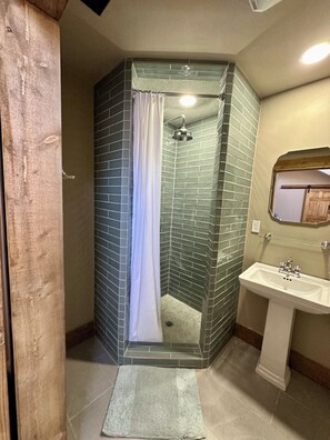 Bathroom features a shower with handheld showerhead and pedestal sink with mirror.