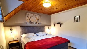 Quarto com cama, mesa de cabeceira, cobertor vermelho, teto de madeira e luzes fixadas na parede.