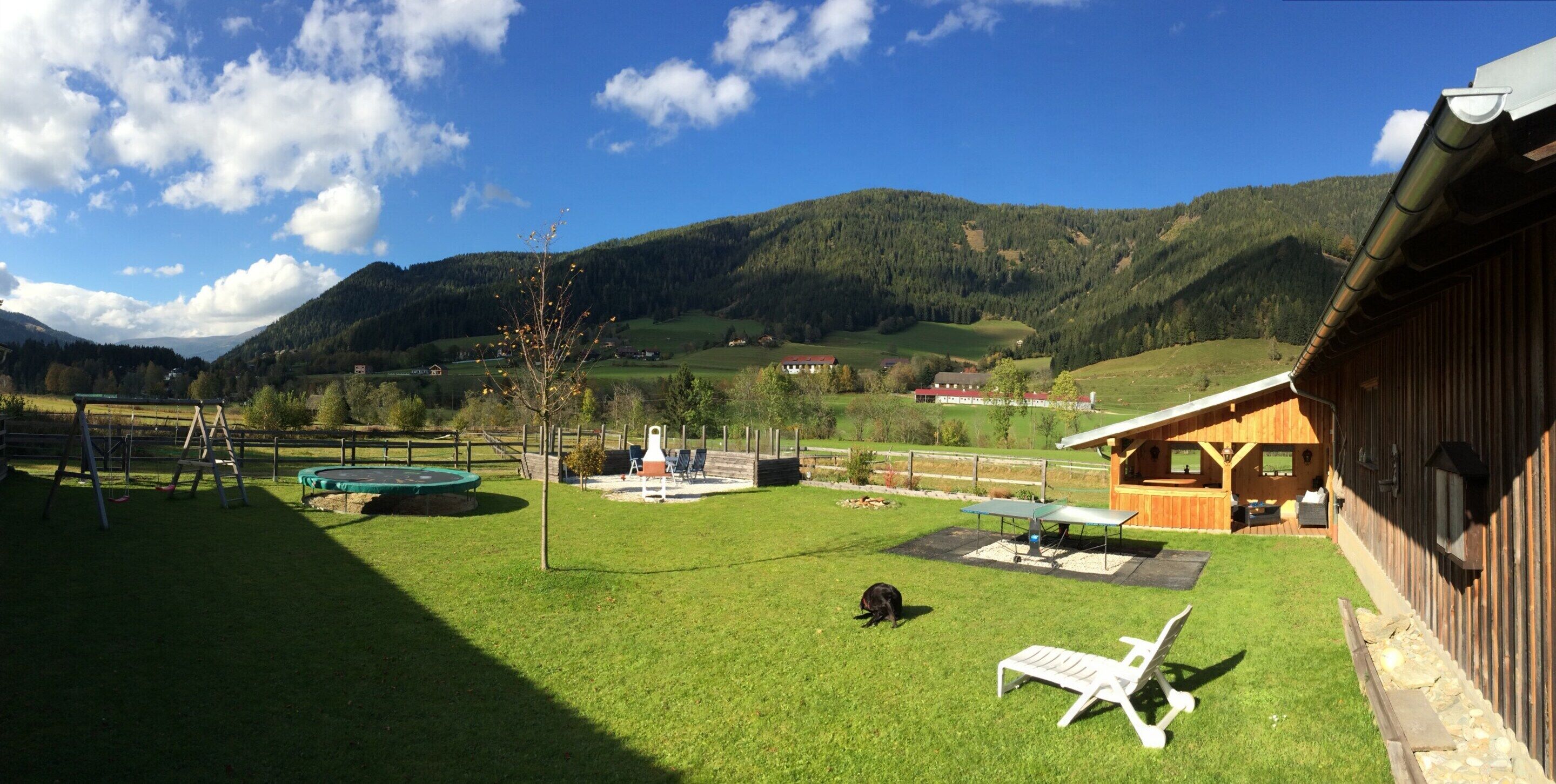 A spacious outdoor area with a wooden cabin, a trampoline, and a picnic table.