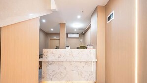 Un área de recepción con mostrador de mármol, paneles de madera e iluminación empotrada en el techo.