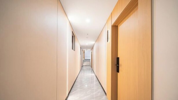 Un pasillo moderno de hotel con piso de mármol, puertas de madera y vista a otra habitación al fondo.