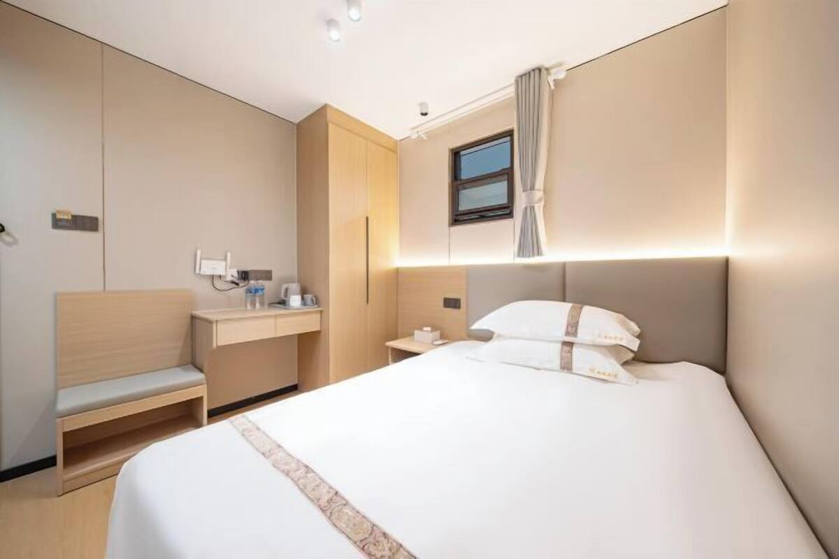 A hotel room with a bed, a bedside table, a chair, a small desk, and a window.