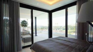 A modern bedroom with a large bed, a view of the outdoors, and a balcony with a chair. - Luxury Villa with Views Marbella  (Marbella)