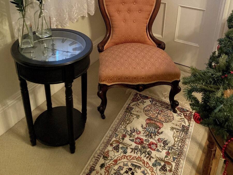 A room with a wooden chair, a small table with a glass top, a floral rug, and a Christmas tree.