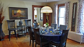 Comedor con una mesa redonda dispuesta para seis comensales, rodeada por seis sillas. Un candelabro ilumina la mesa y un cuadro grande enmarca la pared.