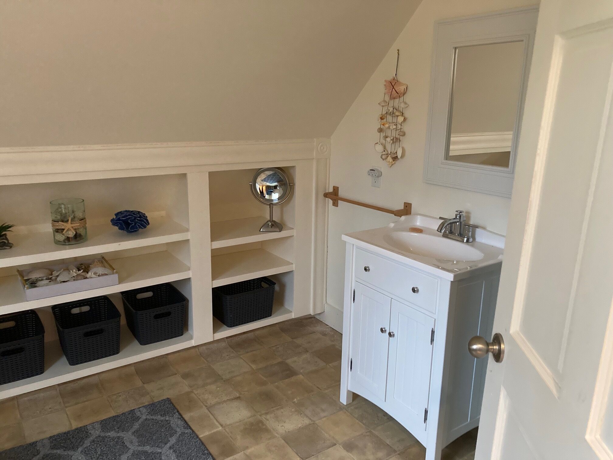 A bathroom with a white vanity, a mirror, and shelves with various items.